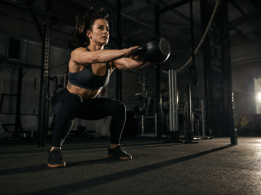Person doing kettlebell swings in a dark gym, dynamic exercise for weight loss